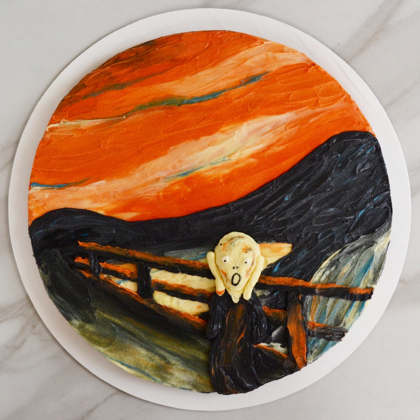 Top-down shot of a circular cake decorated to look like The Scream