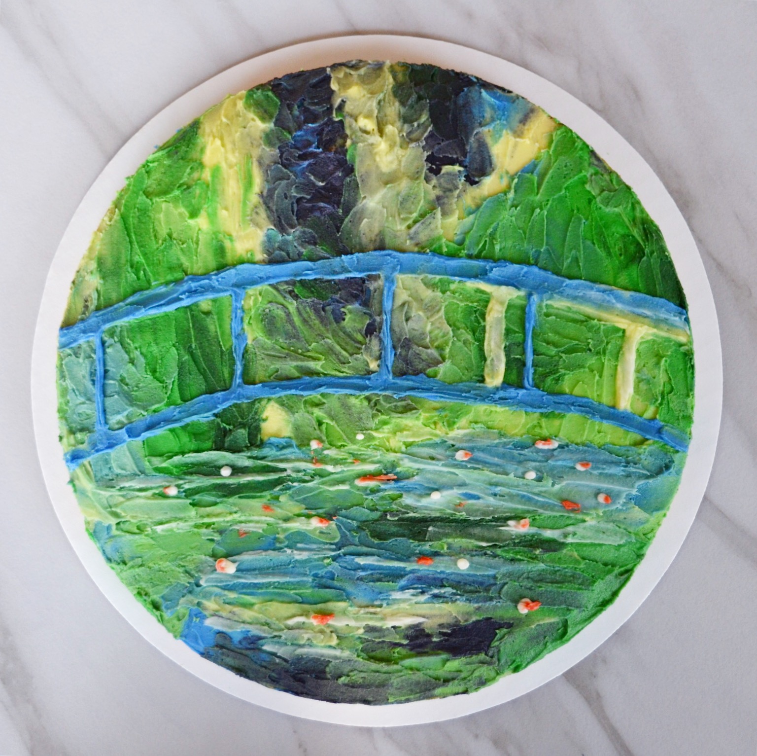 Top-down shot of a circular cake decorated to look like Water Lilies over a Bridge